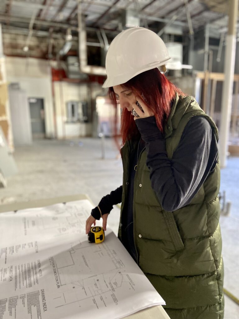 Valentina Lostalo, Owner of Val Spaces, standing in a job site on the phone with architecture plans.